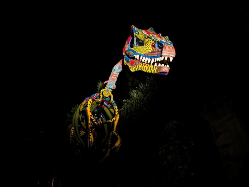 Dinosaure ethnique, spectacle de marionnettes, inspiration Alebrijes, marionnette de scène géante, performance artistique, théâtre de rue Italie, spectacle de dinosaure coloré, performance sur échasses, actes de marionnettes uniques, événements à impact scénique